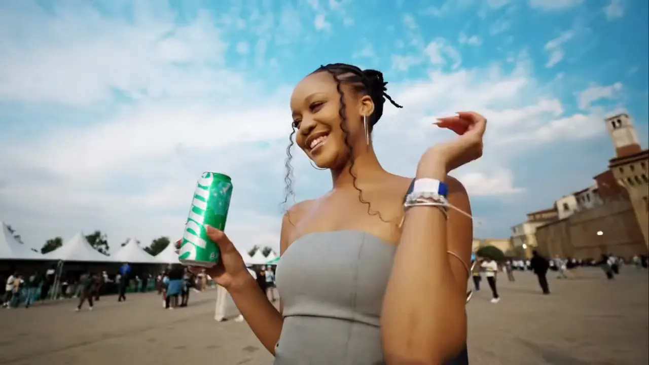 Smiling festival-goer holding a Sprite can under a blue sky