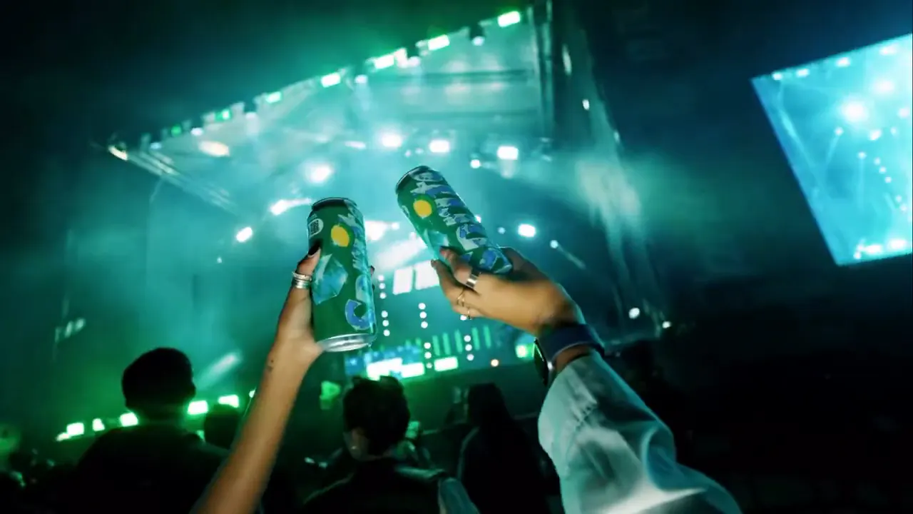 Hands raising two Sprite cans towards a green-lit stage