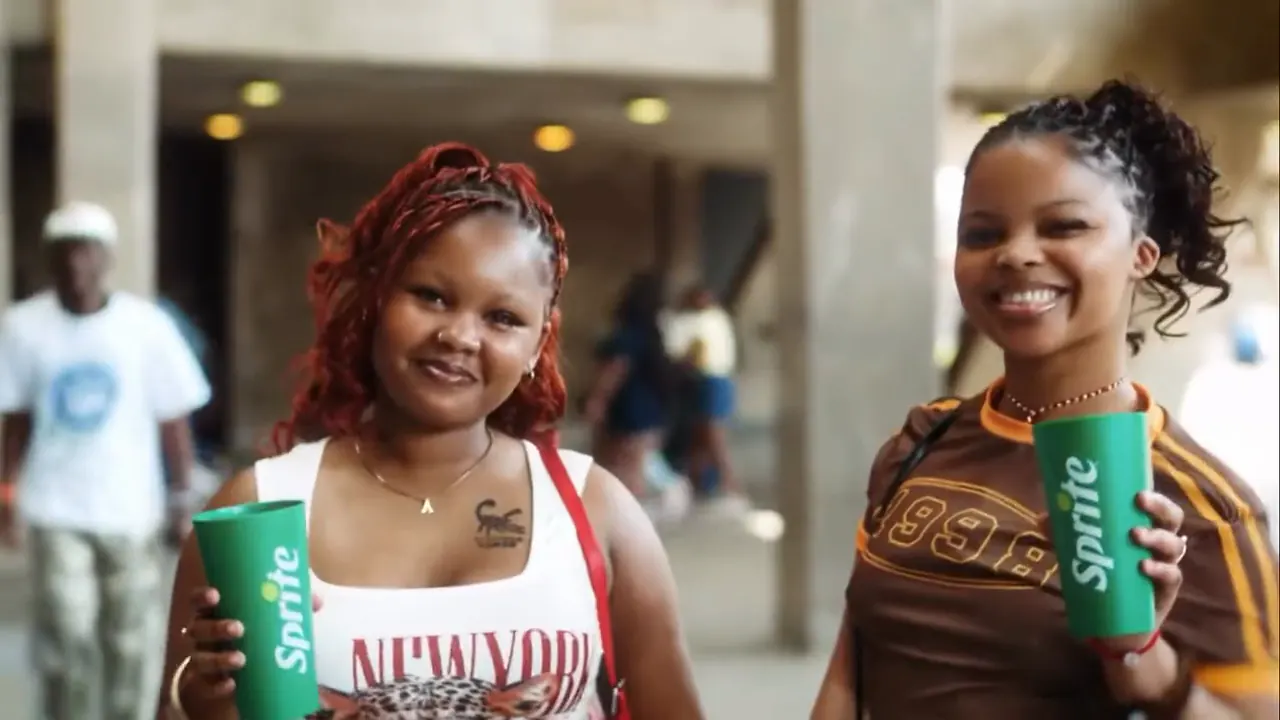 Two fans smiling with green Sprite cups in the stadium concourse