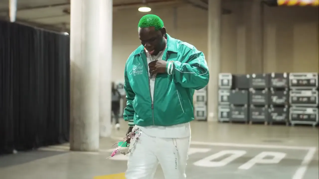 Performer with green hair and a green jacket walking backstage