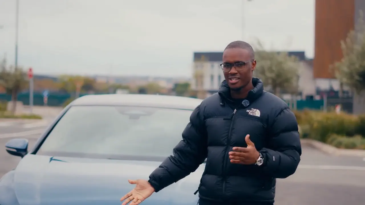 Presenter in a black puffer jacket talking beside the blue Golf GTI