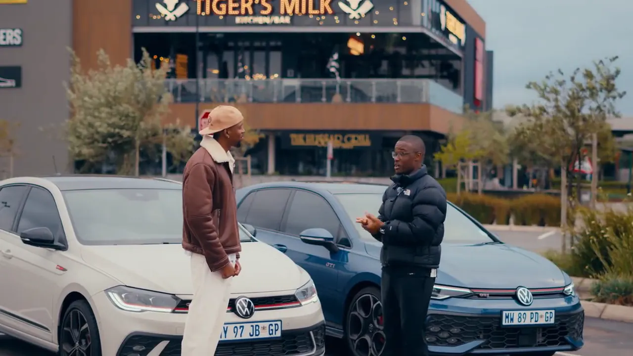 Two presenters talking between a white Polo GTI and a blue Golf GTI